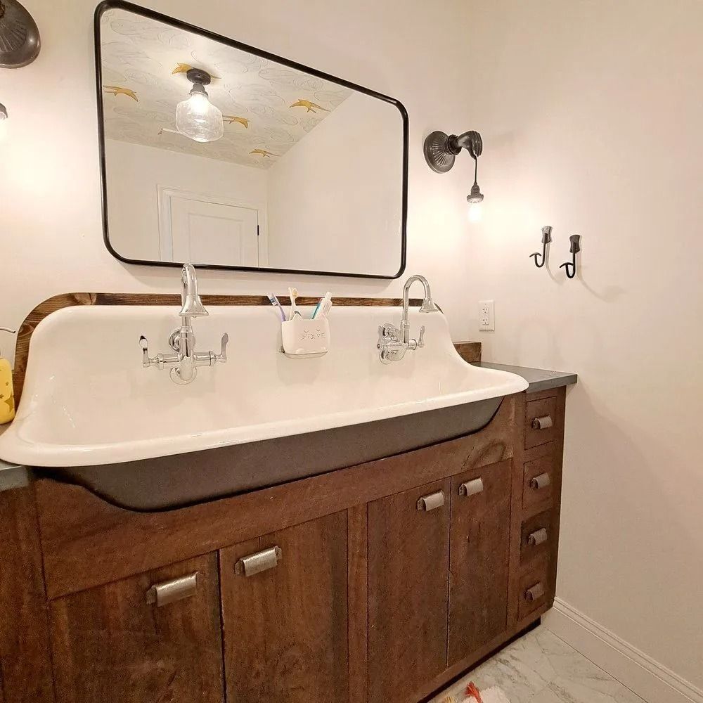 Bathroom with a long, white, vintage sink on a wooden cabinet, black-framed mirror, and sconce lighting.
