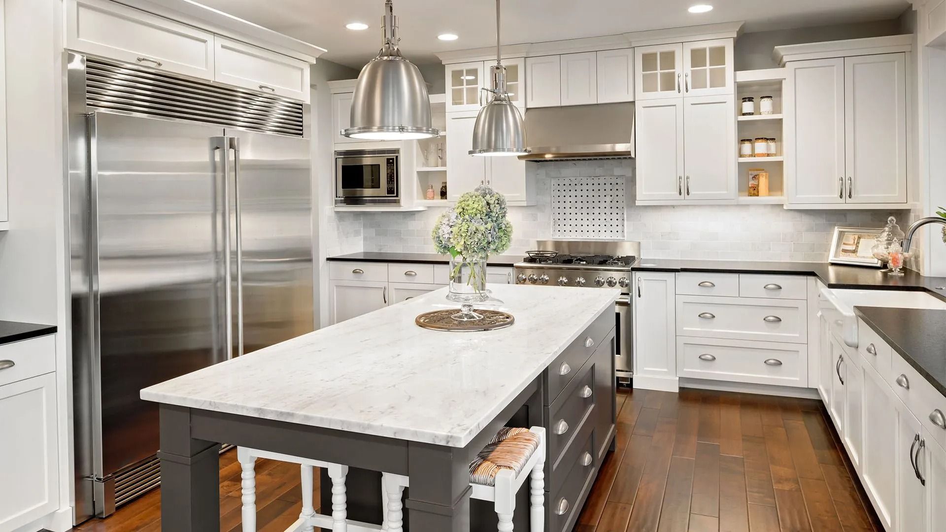 White kitchen with island, stainless steel appliances, and dark wooden floors.