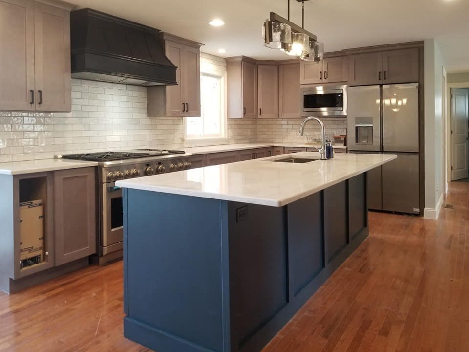 Modern kitchen with gray cabinets, navy island, stainless steel appliances, and white countertops.