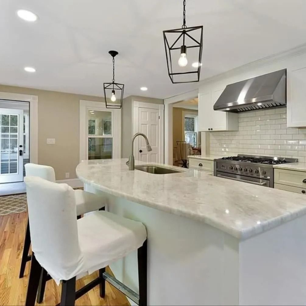 Modern kitchen with marble island, white cabinets, stainless steel range, and pendant lights.