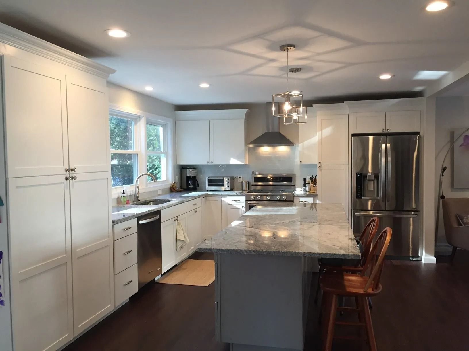 White kitchen with stainless steel appliances, marble countertops, and a wooden island.