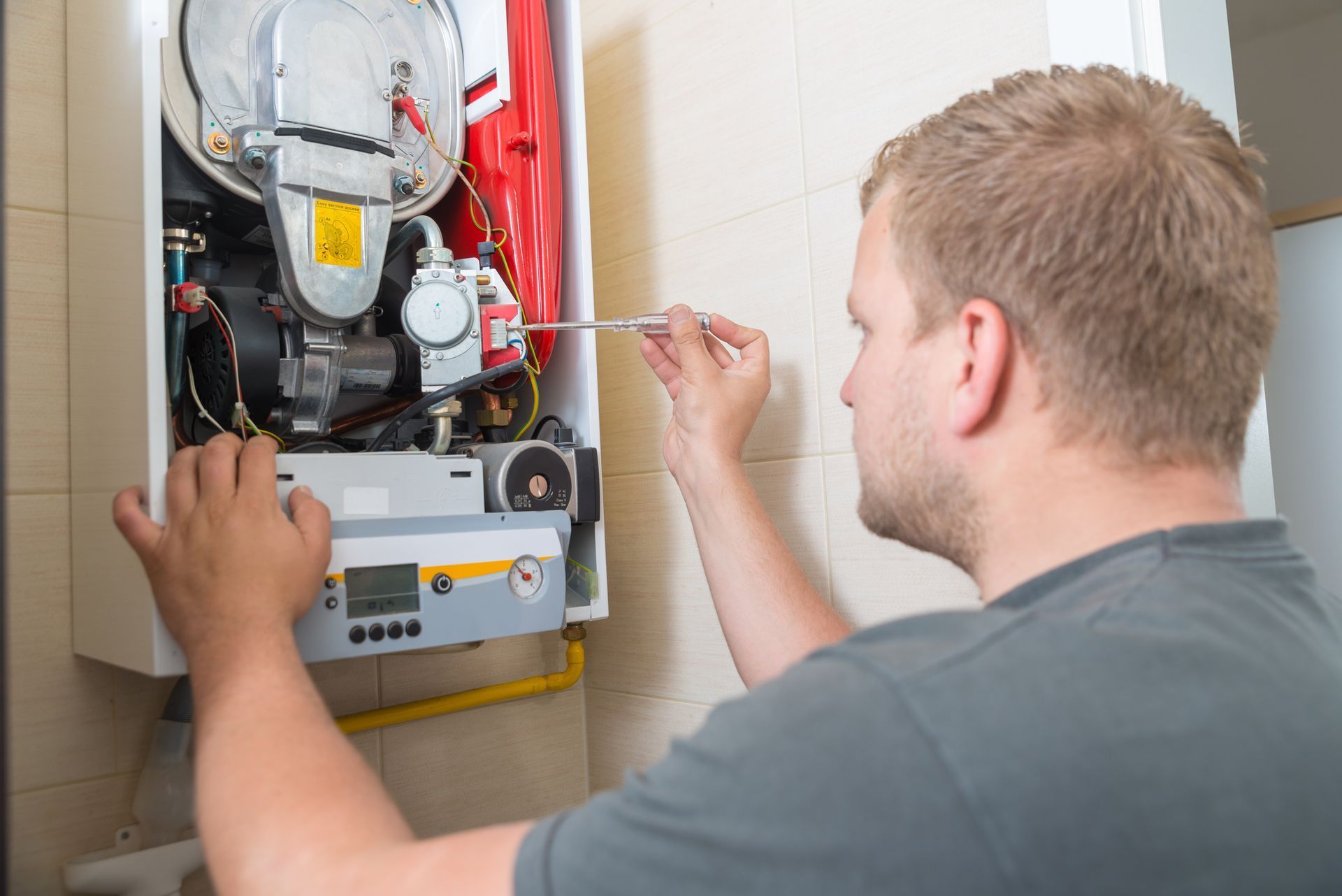 Technician adjusting wiring inside an open wall-mounted boiler or heater unit