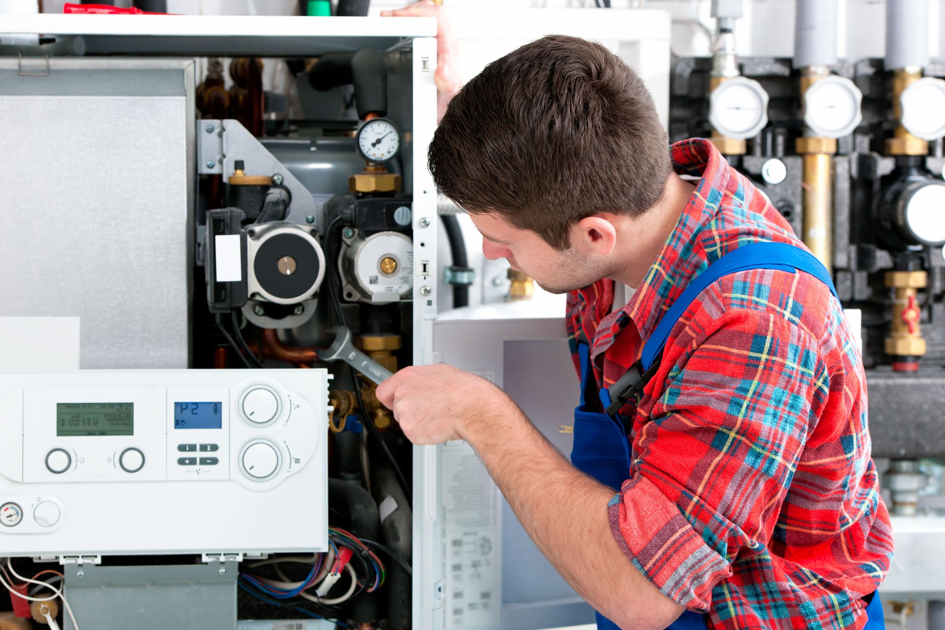 Technician inspecting an open boiler control panel with tools in a mechanical room