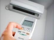 Hand holding a remote control aimed at a wall-mounted air conditioner