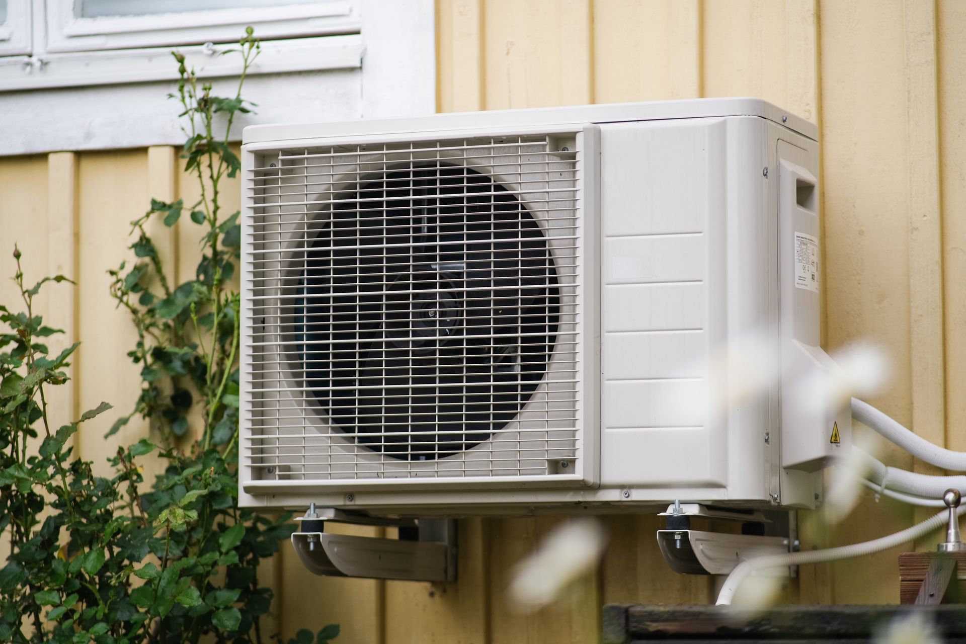 Outdoor air conditioning unit mounted on a wall beside a window and house siding