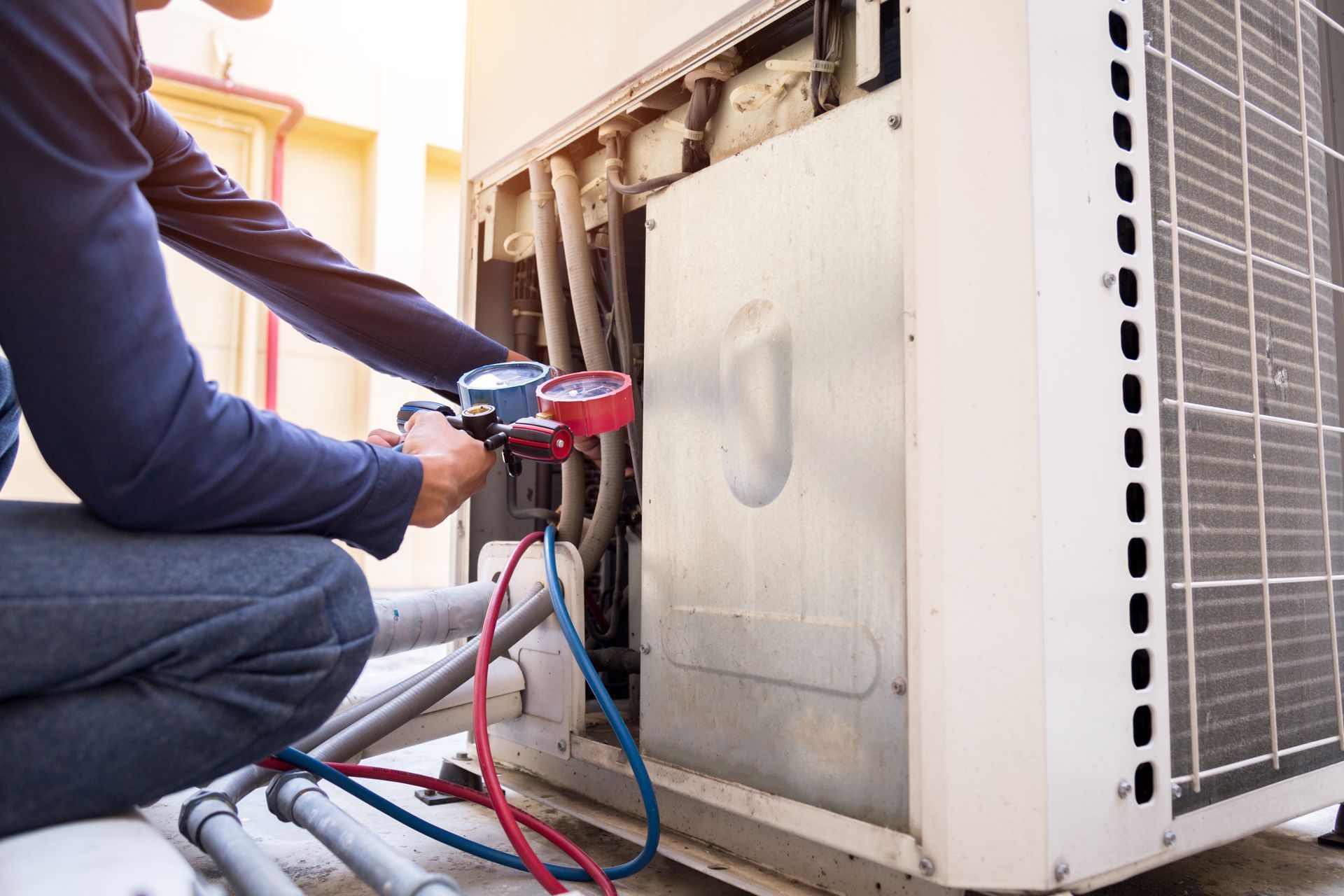 Technician using a gauge on an outdoor HVAC unit during maintenance