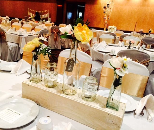 Wedding reception decor: floral centerpieces in a wooden box on a table with white tablecloth and gold accents.
