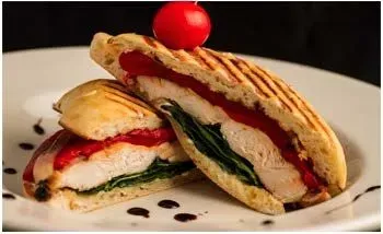 Panini sandwich, grilled bread, chicken, spinach, red pepper, tomato garnish on a white plate.