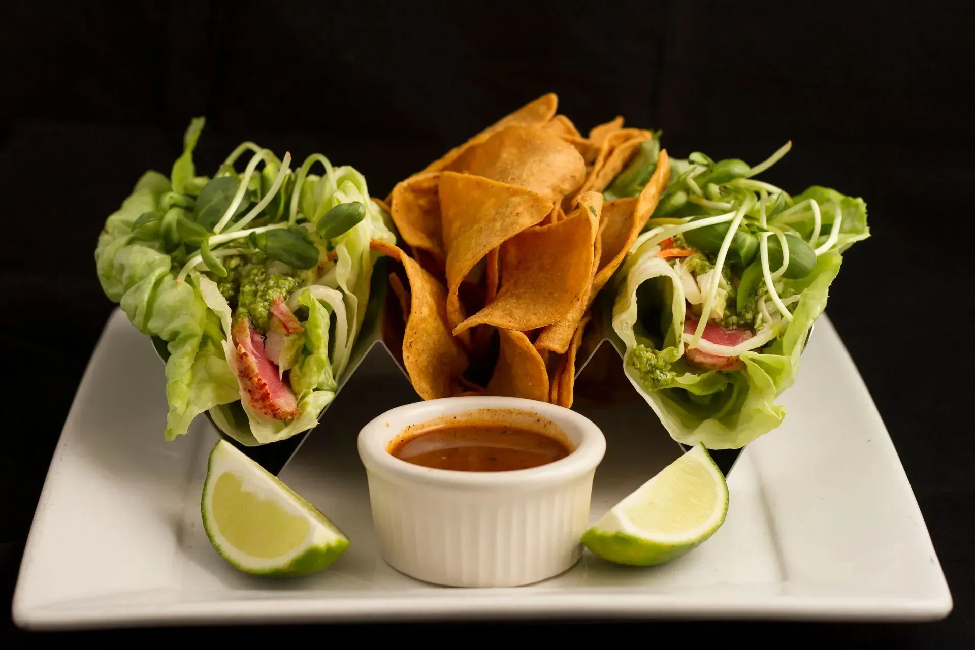 Plate of lettuce wraps and tortilla chips with dipping sauce and lime wedges.