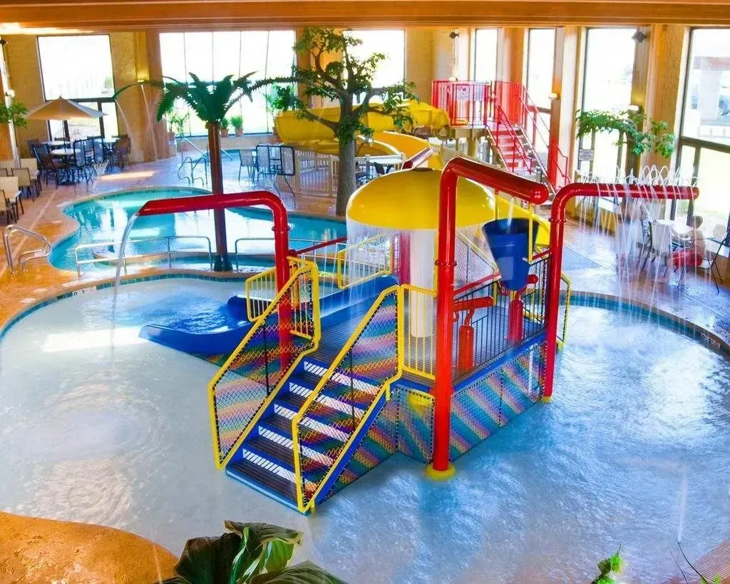 Indoor waterpark with slides, play structures, palm trees, and tables.