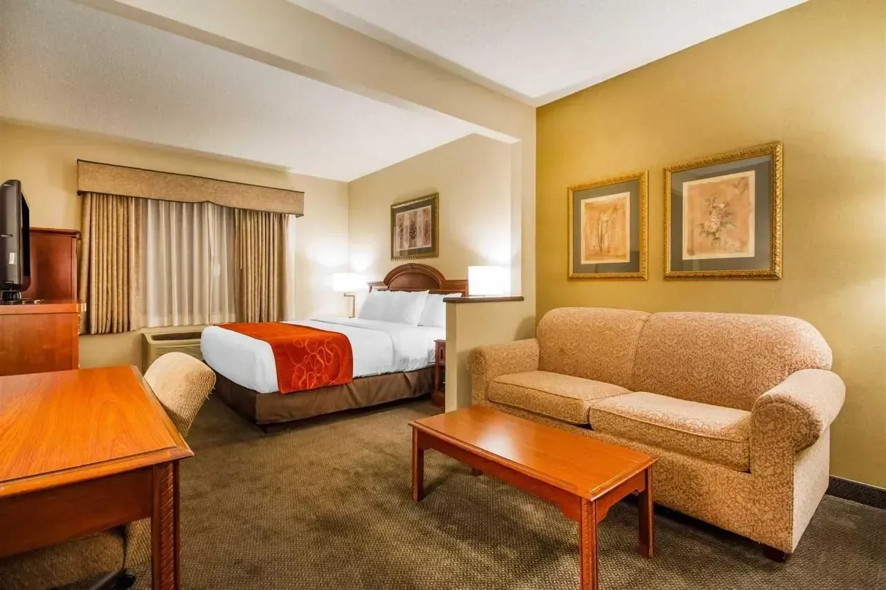 Hotel suite with a bed, couch, desk, and two framed prints.