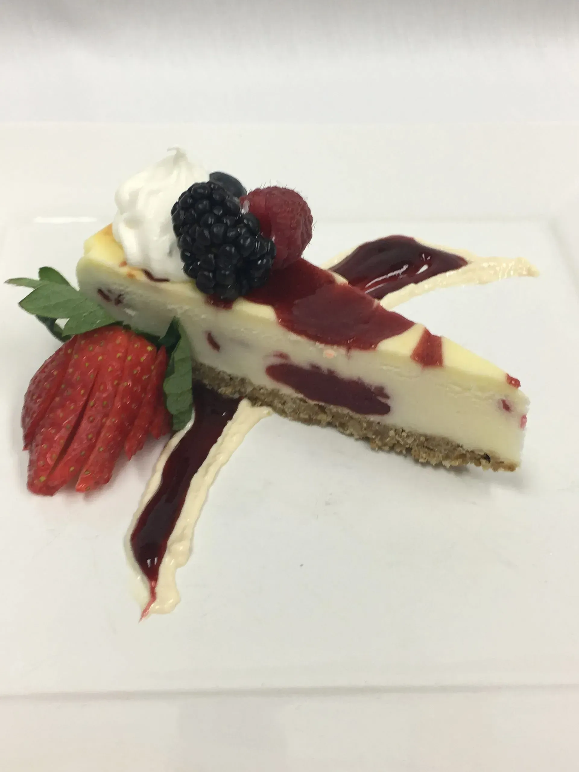 Slice of cheesecake with berries, whipped cream, and sauce on a white plate.