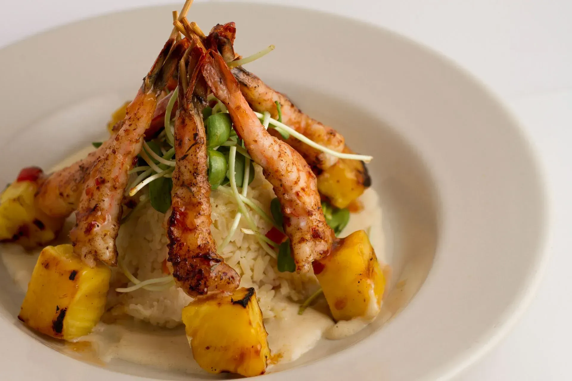 Grilled shrimp skewers with pineapple chunks atop rice and sauce on a white plate.