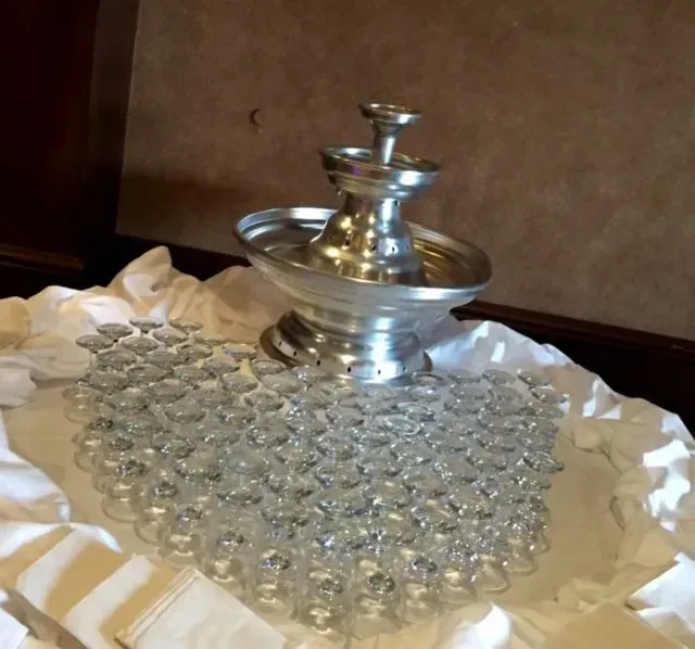 Champagne fountain with cascading liquid over stacked glasses. White cloth covers the table.