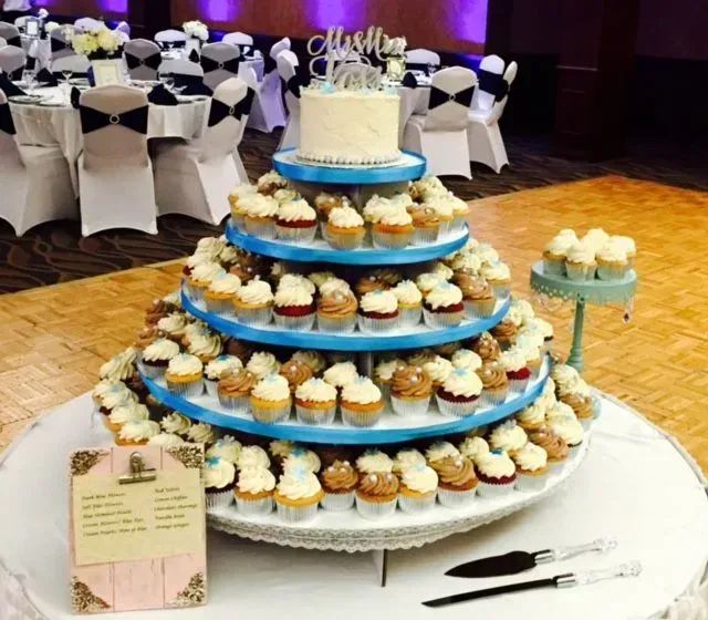 Wedding cupcake tower with small cake on top; decorated with teal accents, in a banquet hall.