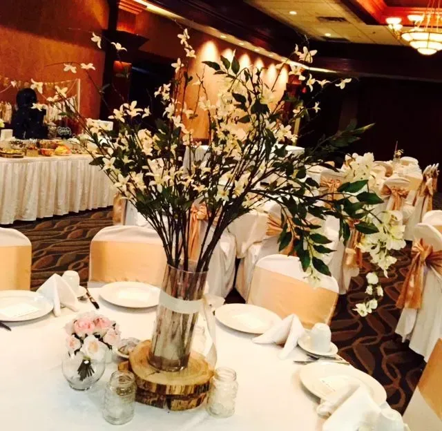 Wedding reception table with floral centerpieces, white tablecloths, and peach chair sashes.