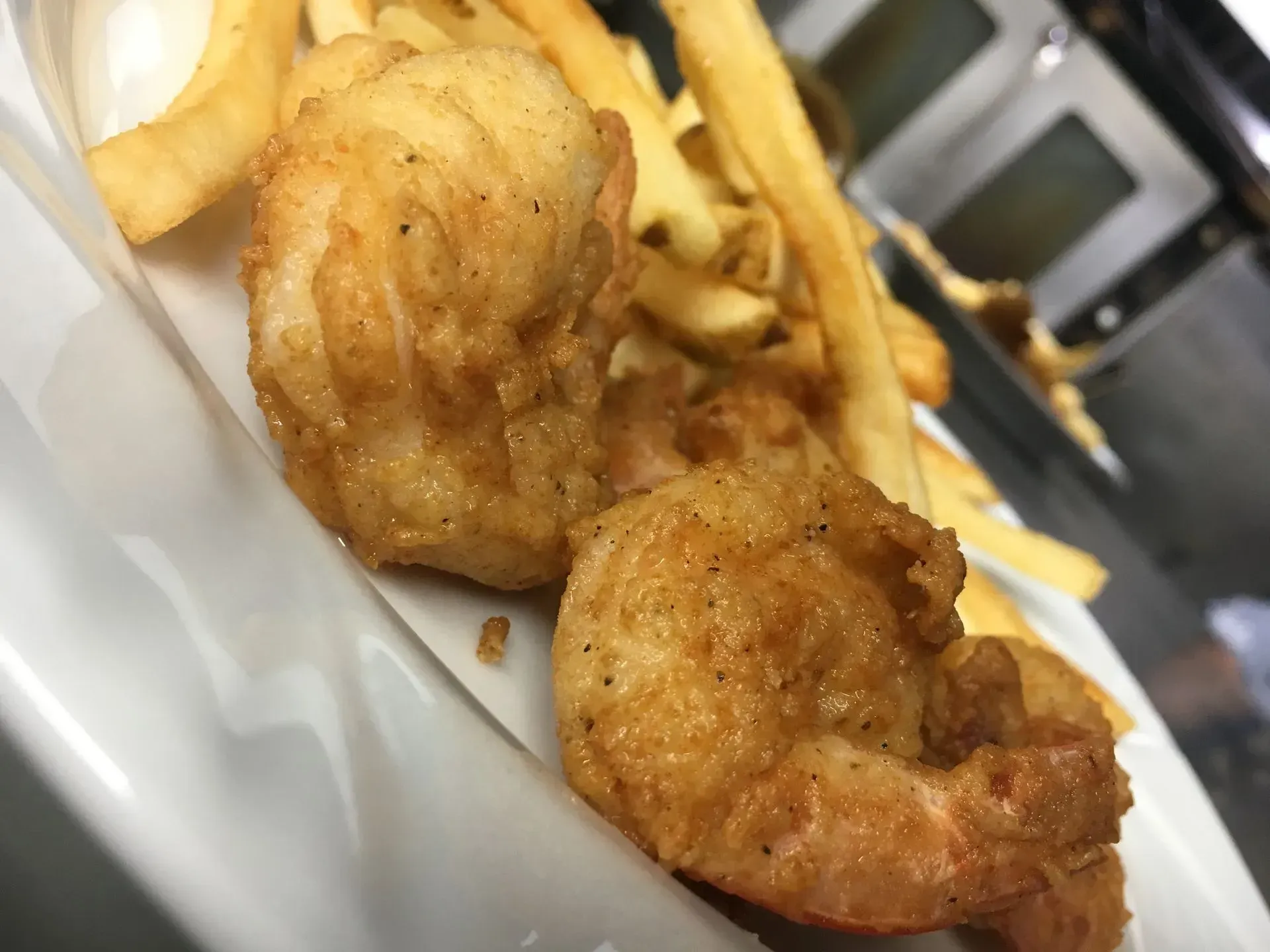 Fried shrimp and french fries on a white plate, close-up shot.