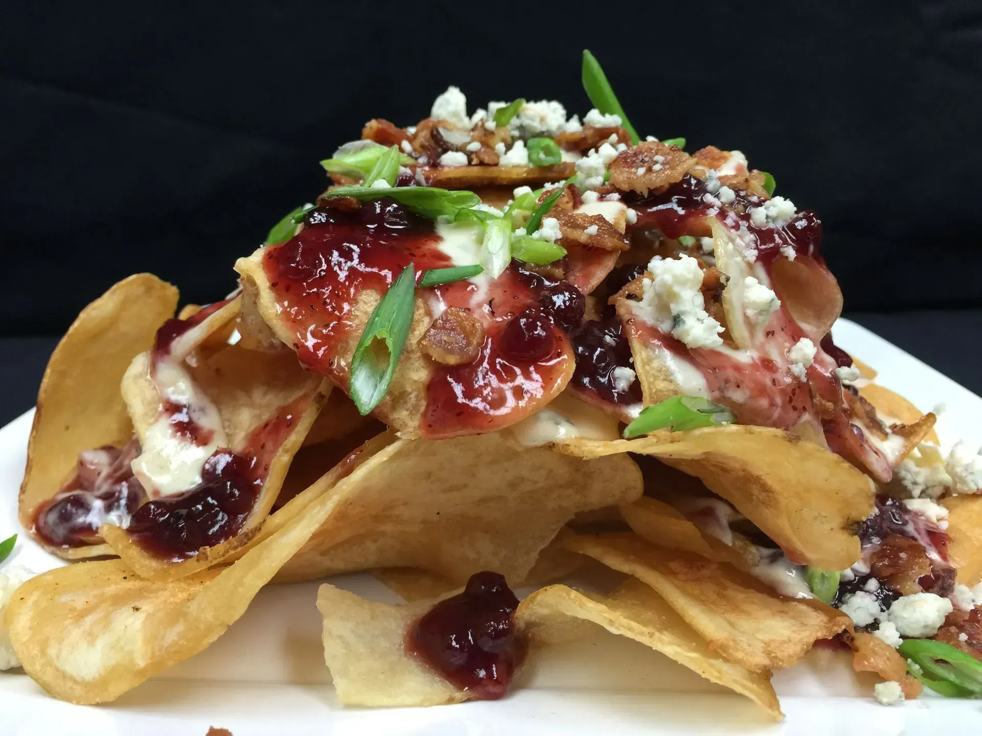 Pile of potato chips topped with sauce, blue cheese, bacon, and green onions on a white plate.