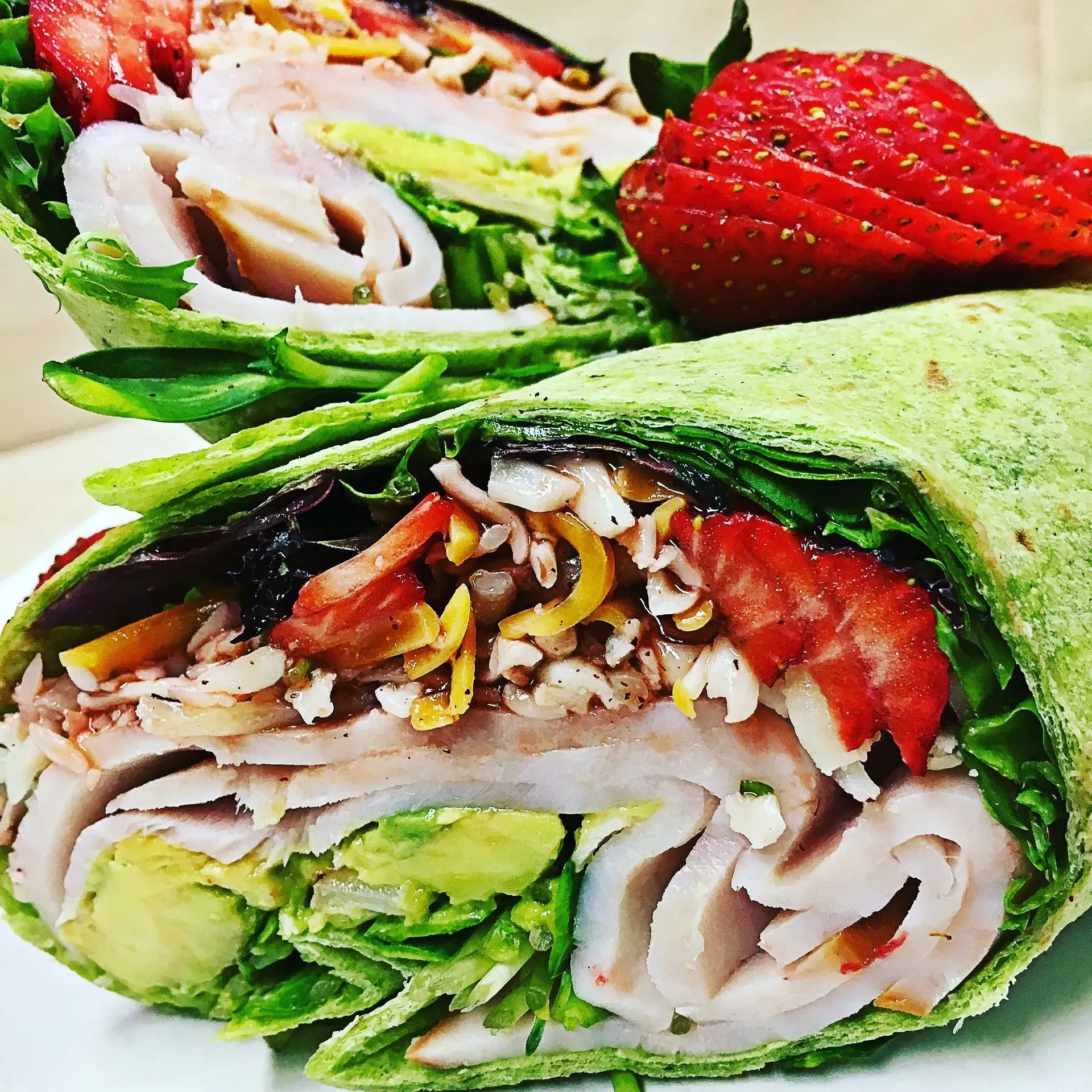 Green spinach wrap filled with turkey, avocado, lettuce, cheese, and strawberries.