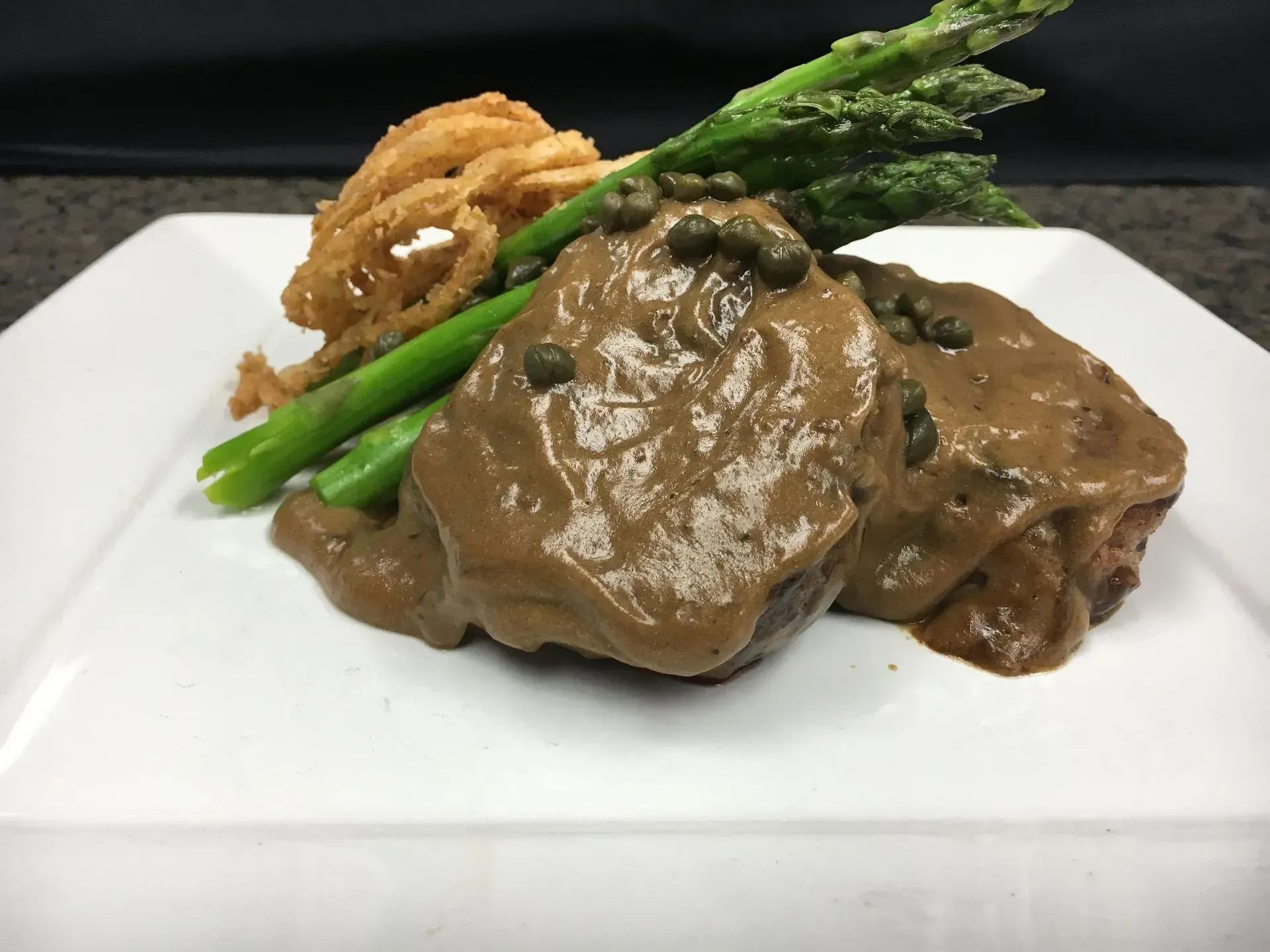Steak with mushroom sauce, asparagus, and onion rings on a white plate.