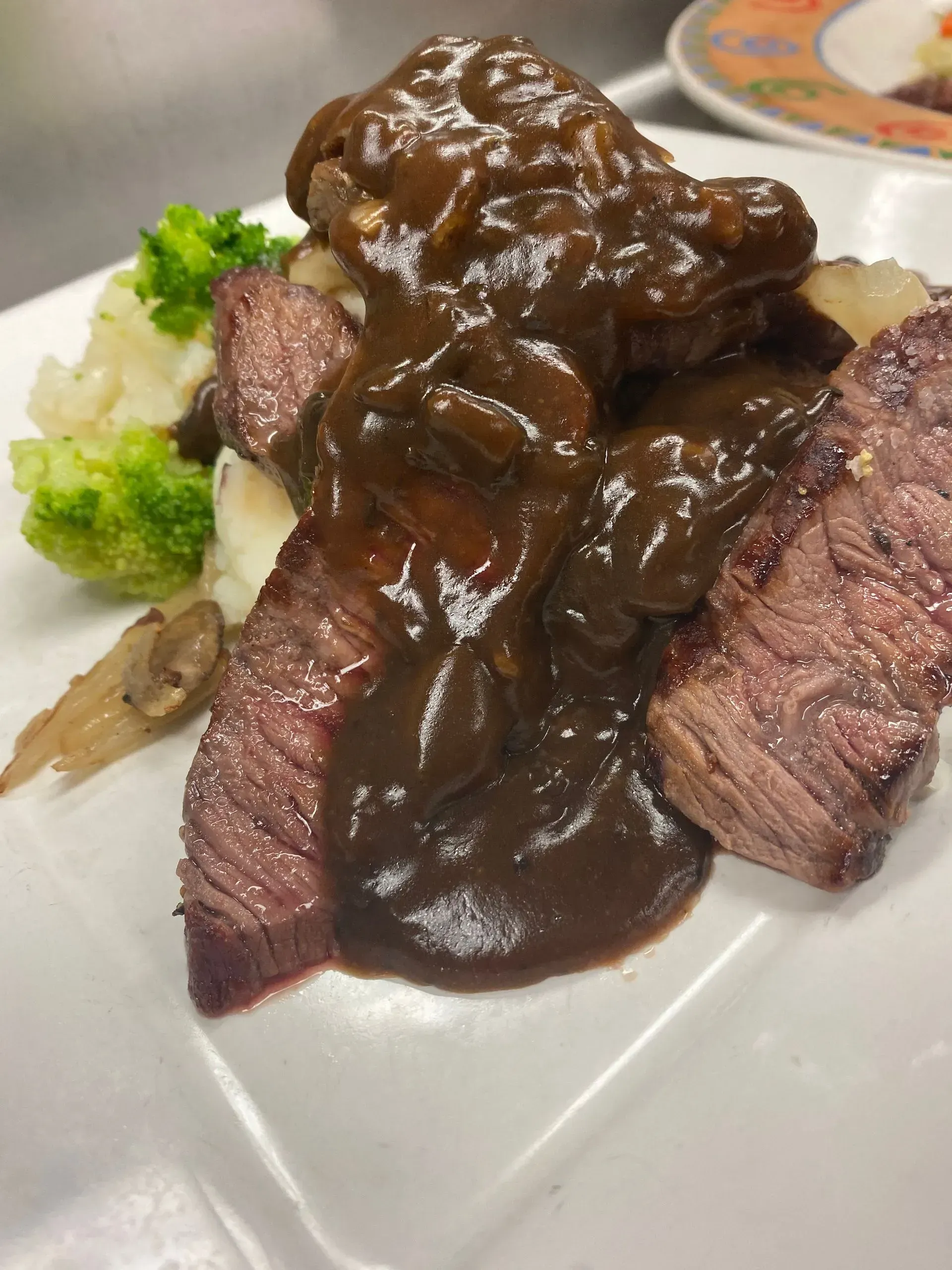 Steak with gravy, mashed potatoes, and broccoli on a white plate.