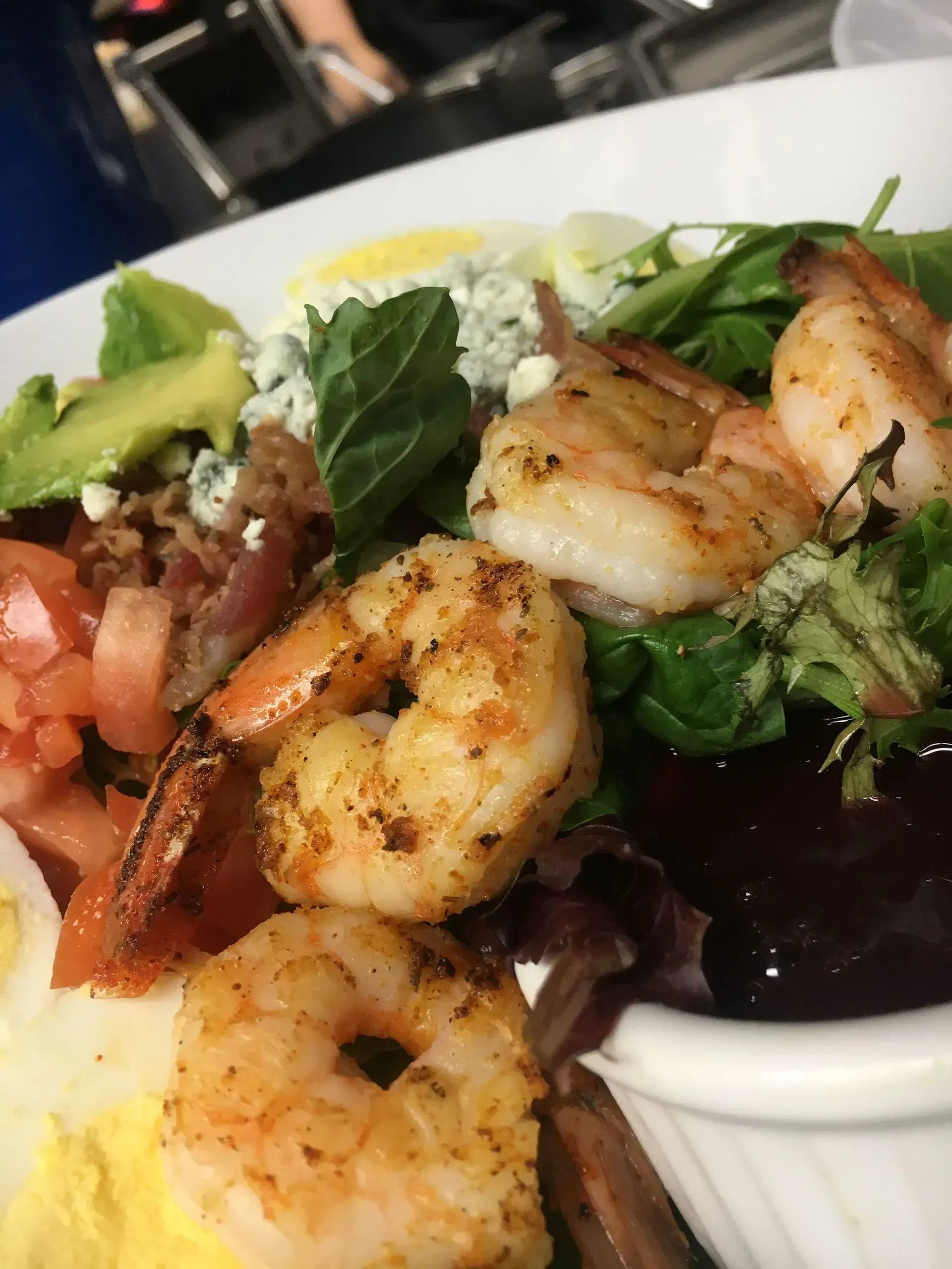 Shrimp salad with avocado, tomato, egg, bacon, and blue cheese on a white plate.