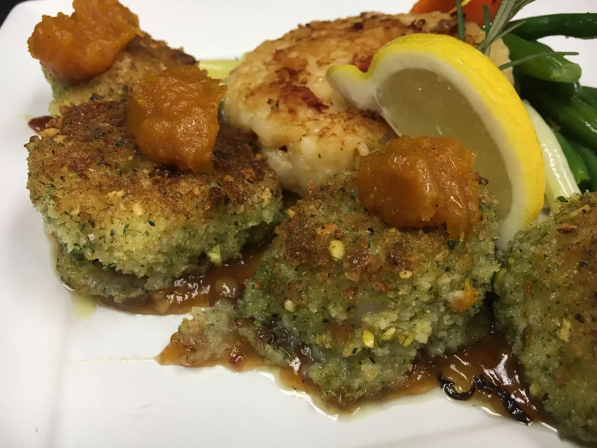 Plated fish dish: breaded patties with sauce, seared fillet, lemon wedge, and green beans.