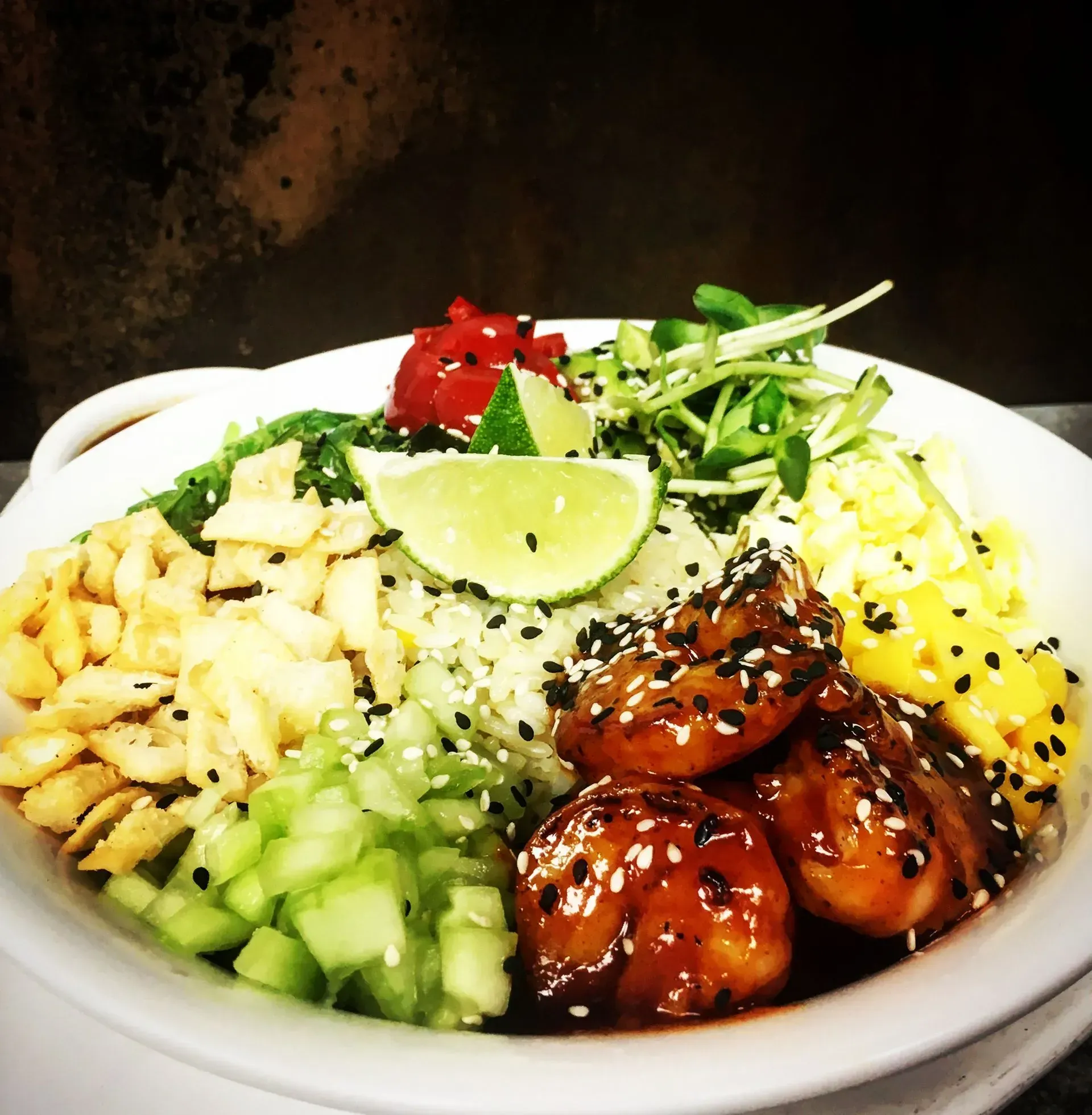 Bowl with rice, chicken, vegetables, and lime, sprinkled with sesame seeds.