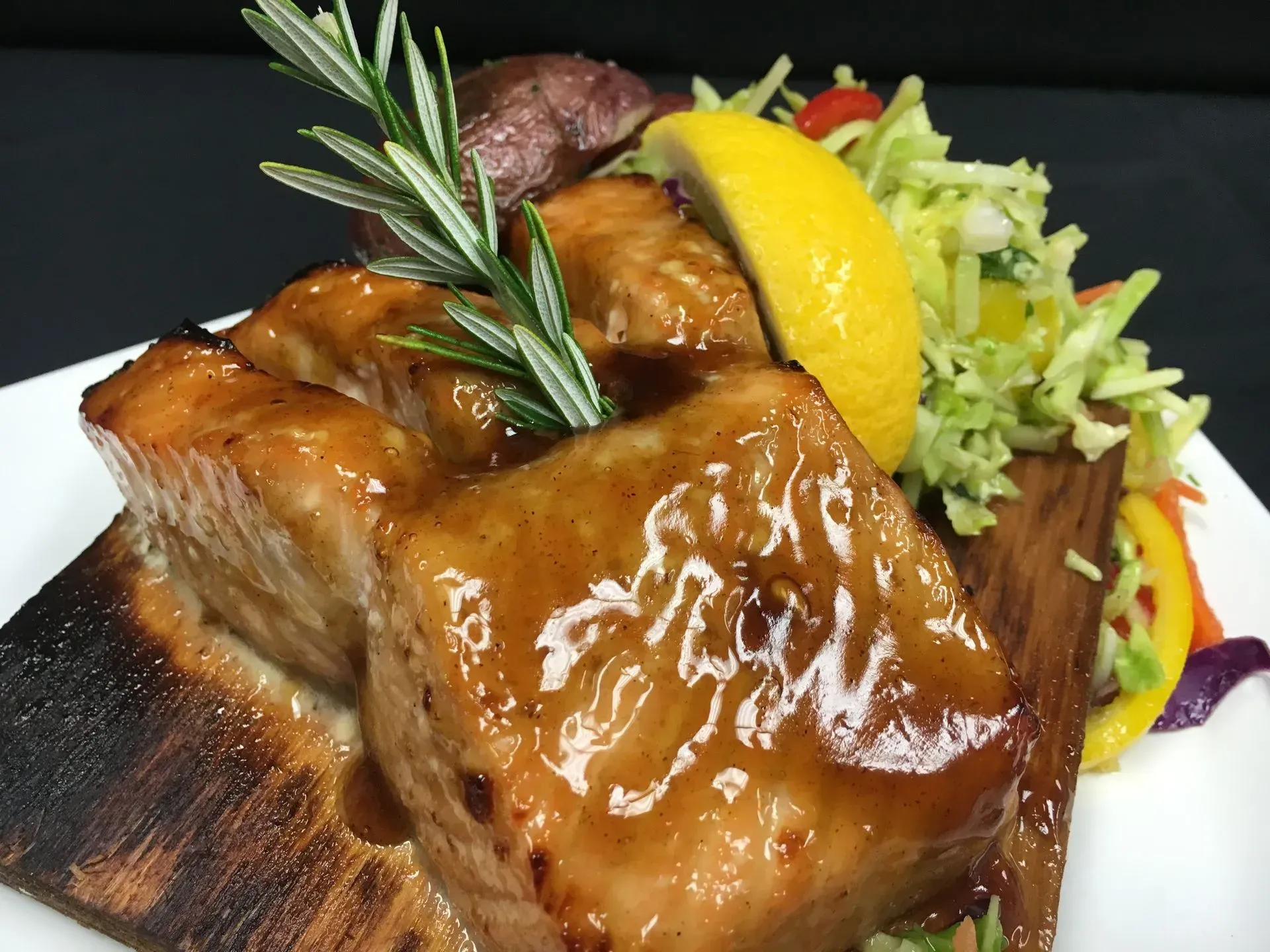 Grilled salmon bites with glaze, lemon, and slaw on a wooden plank.