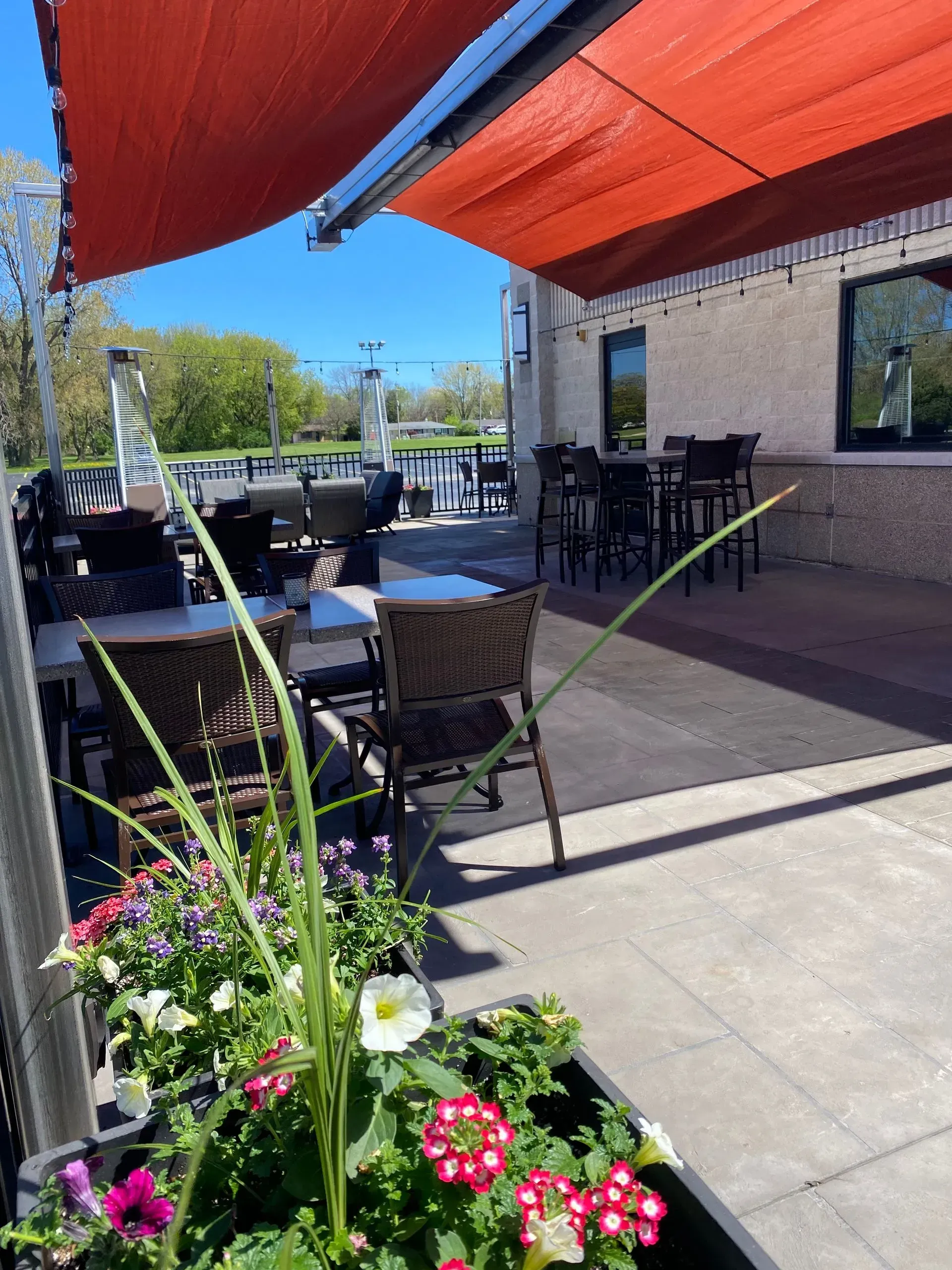 Outdoor patio with tables and chairs under a red awning, flowers in a planter.