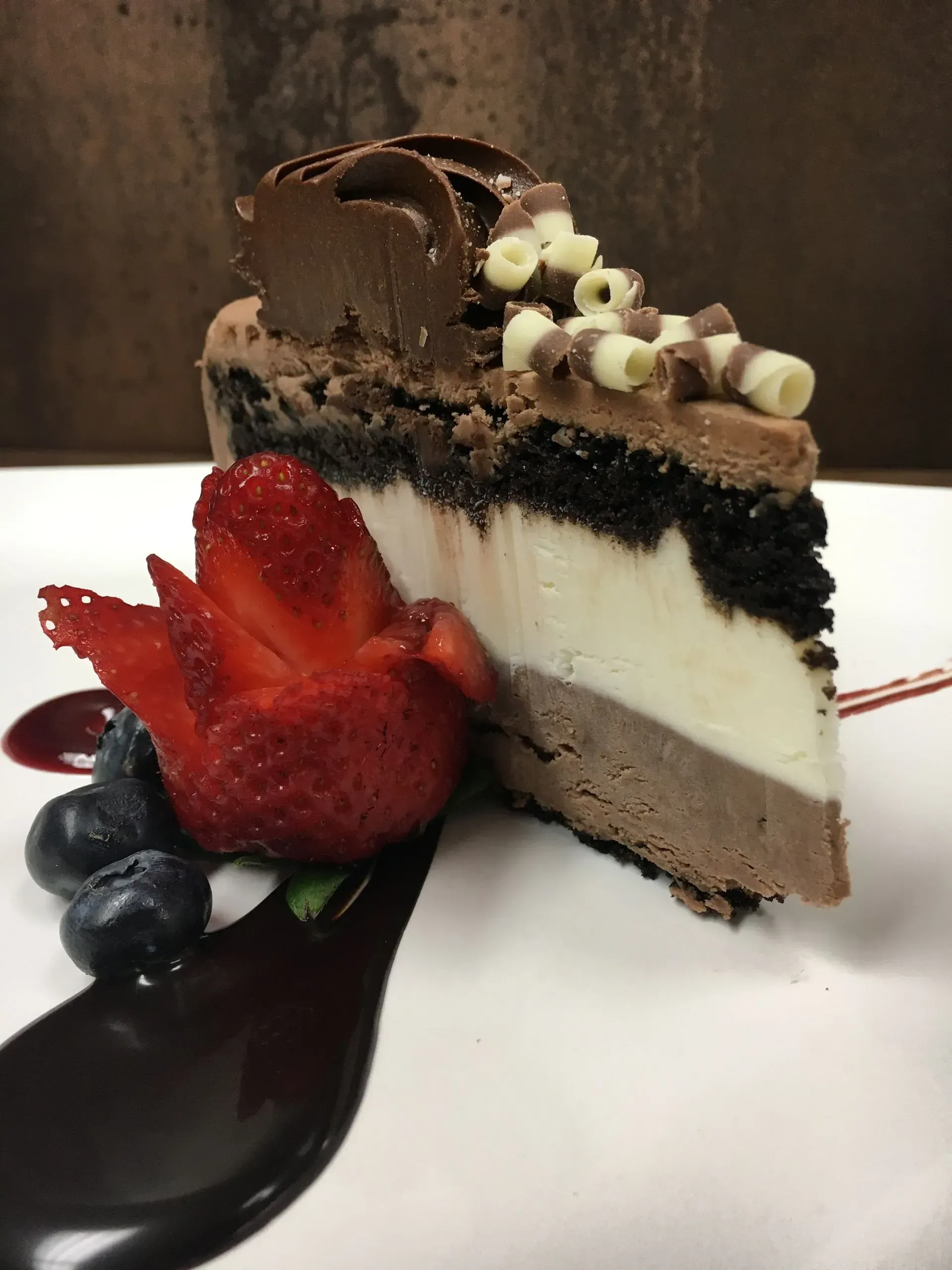 Slice of layered chocolate dessert with fruit garnish on a white plate.