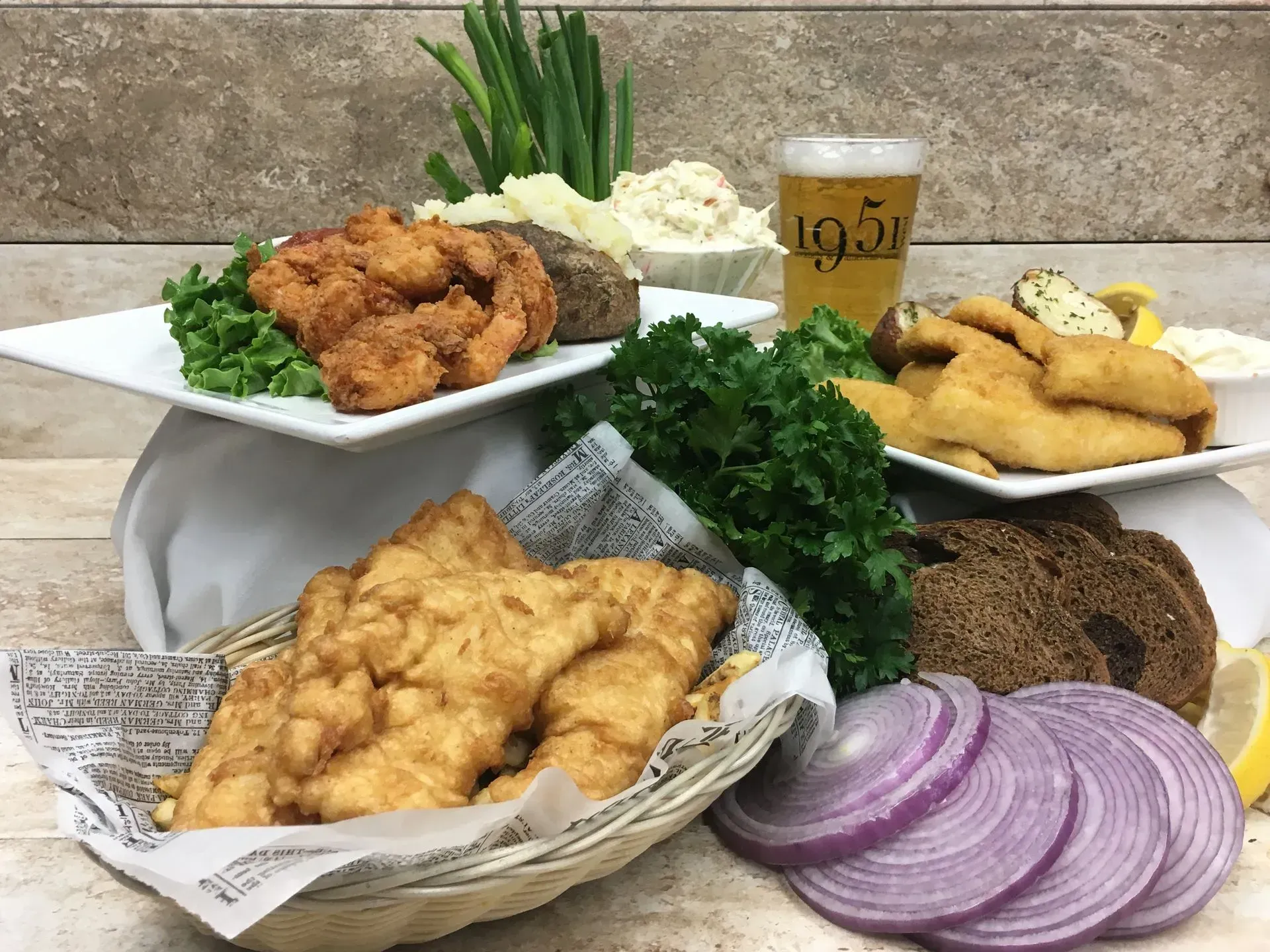 Platters of fried fish, side dishes, beer, and sliced onions; a restaurant setting.