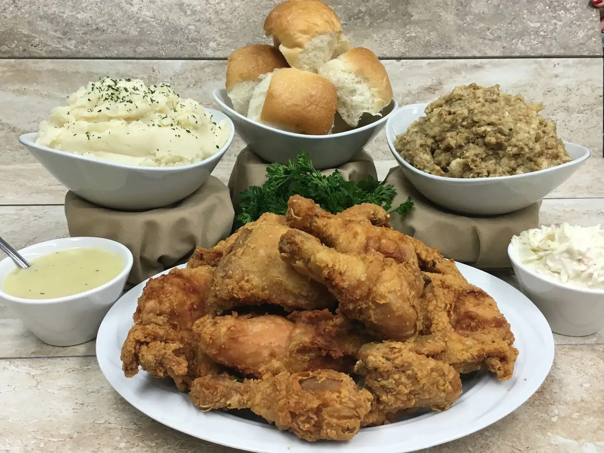 Fried chicken platter with sides: mashed potatoes, rolls, stuffing, gravy, and coleslaw.