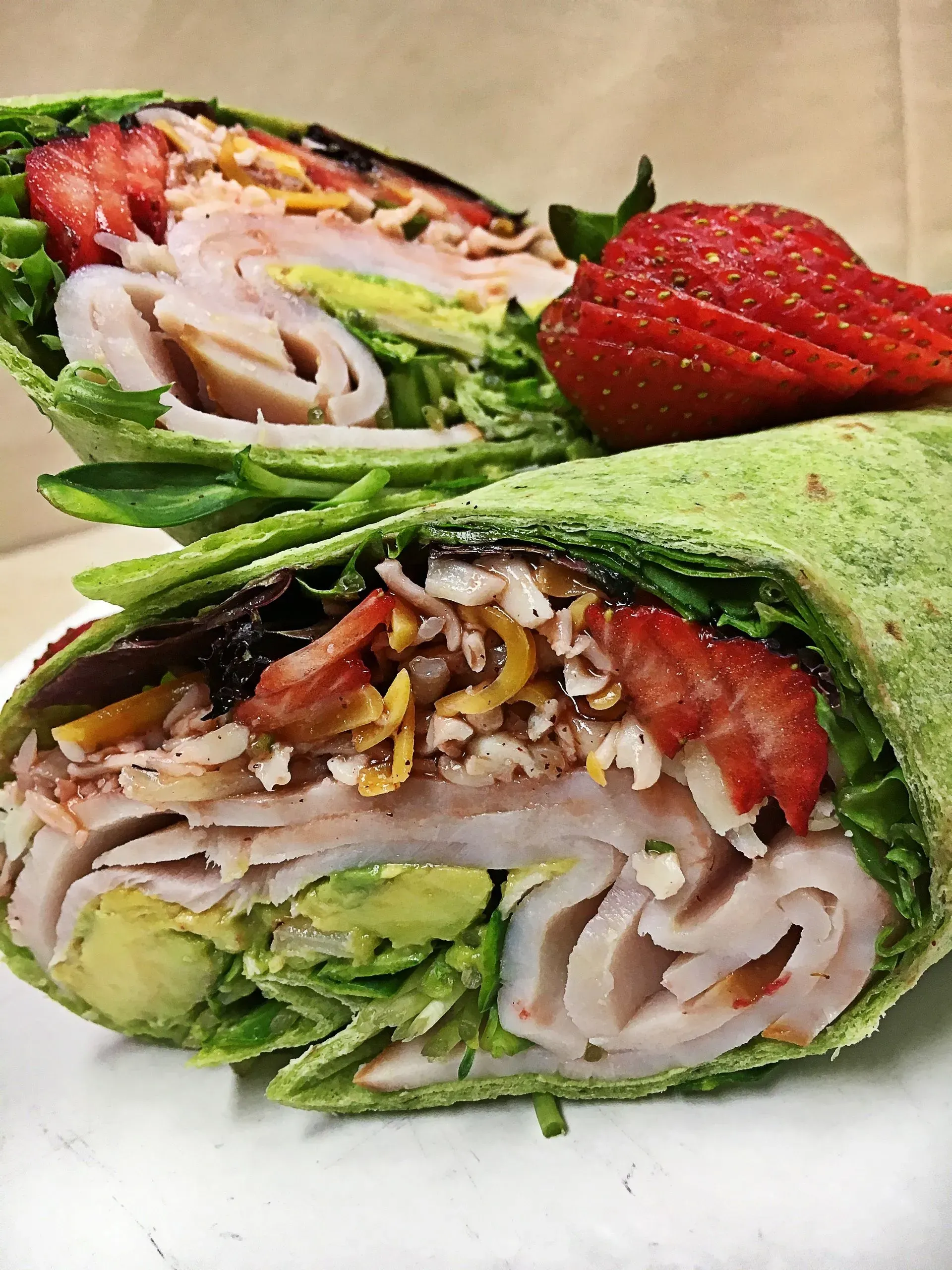 Green wrap sandwich with turkey, avocado, lettuce, strawberries, and cheese.