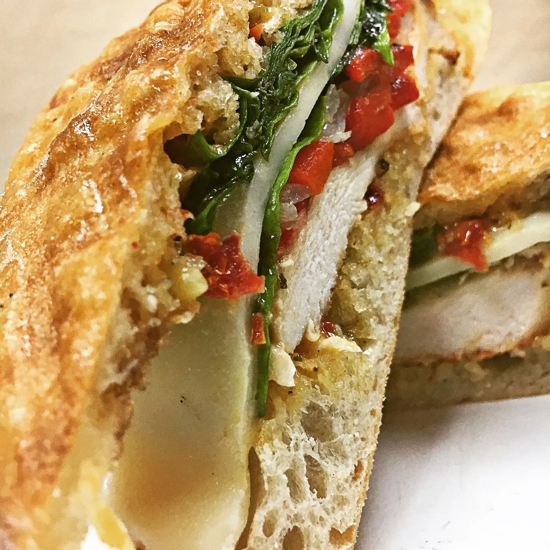 Grilled sandwich cut in half, showcasing chicken, cheese, red peppers, and greens.