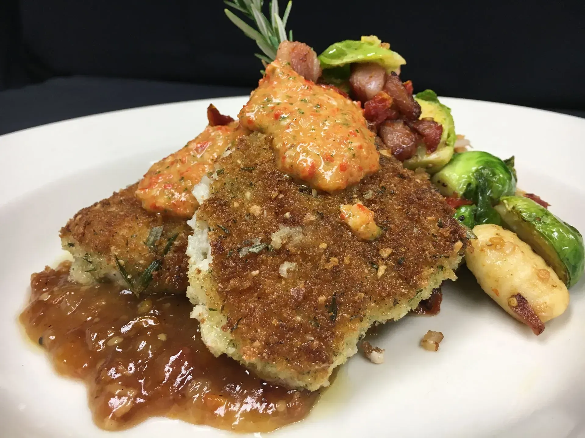 Fried fish with sauce and vegetables on a white plate.