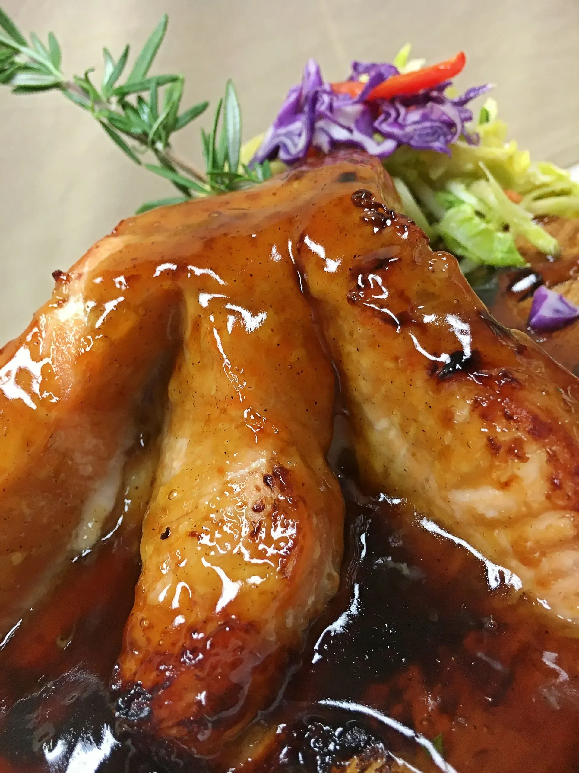 Chicken wings in glossy sauce, topped with slaw and rosemary sprig.