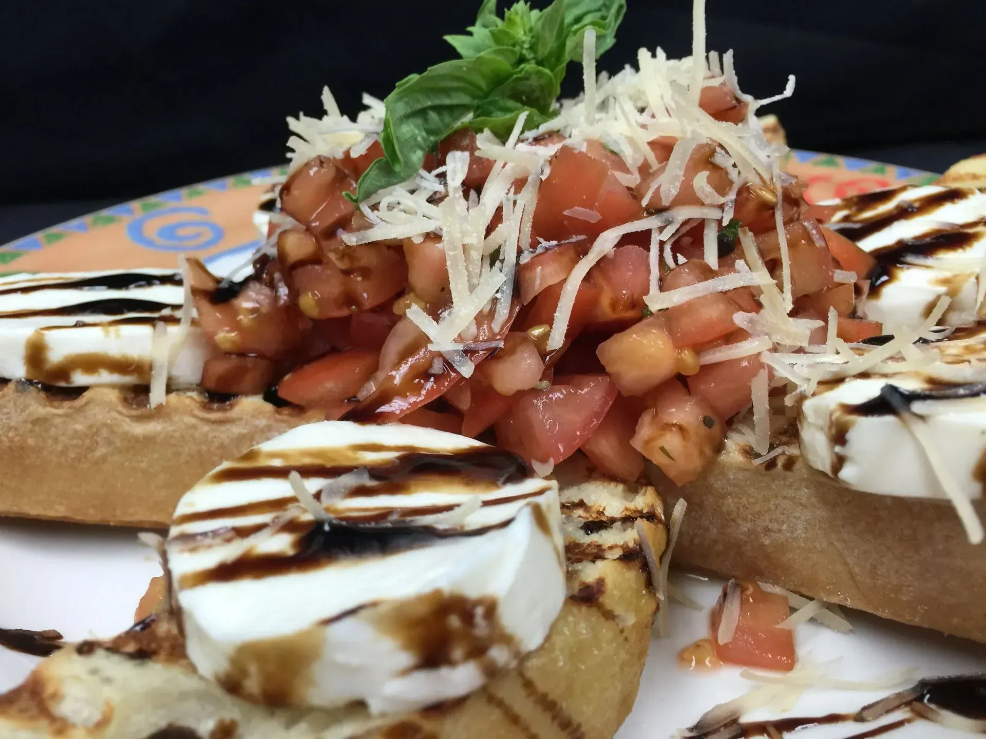 Bruschetta appetizer with diced tomatoes, mozzarella, balsamic glaze, and grated cheese on toasted bread.