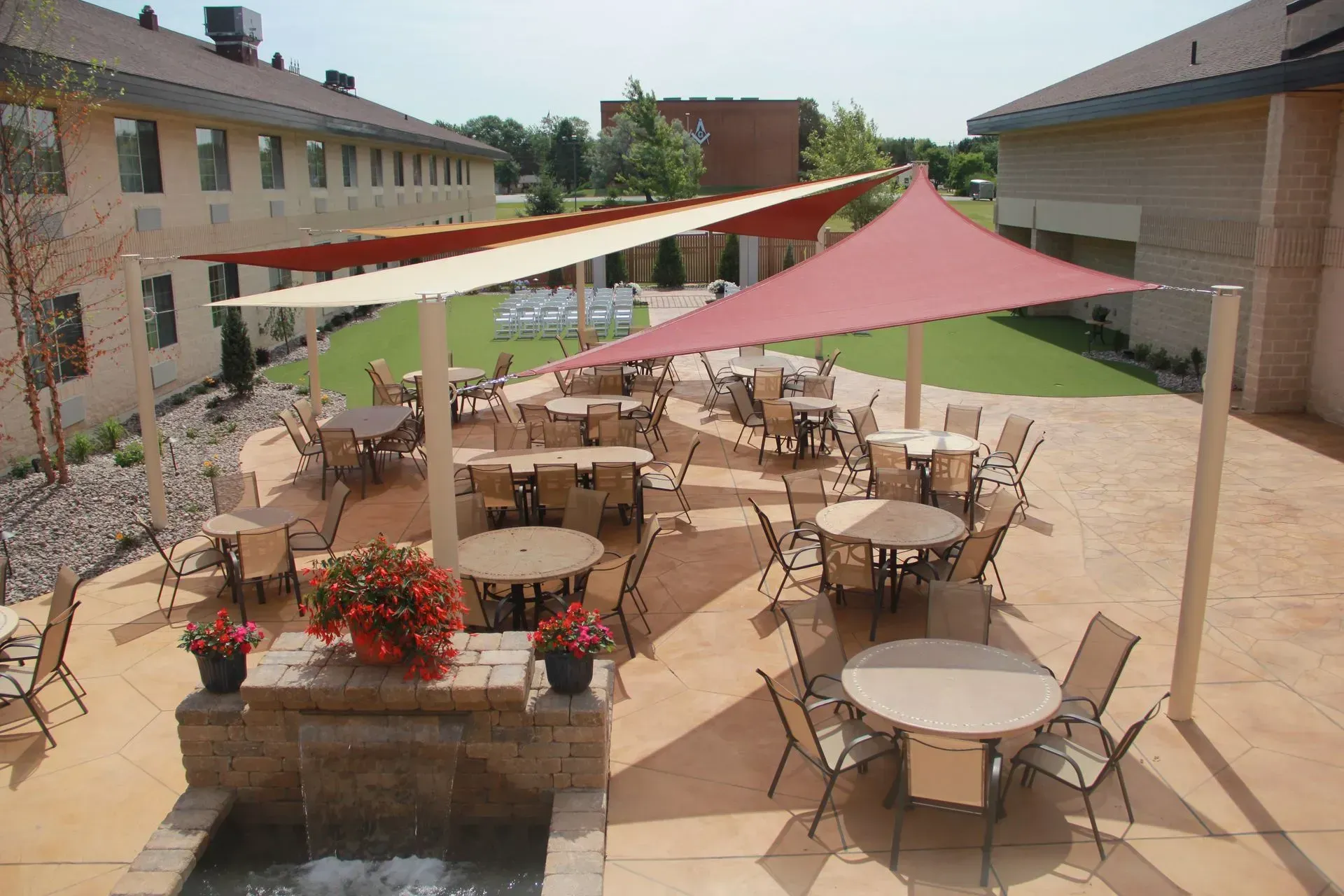 Outdoor patio with tables, chairs, and shade sails. Building in the background.