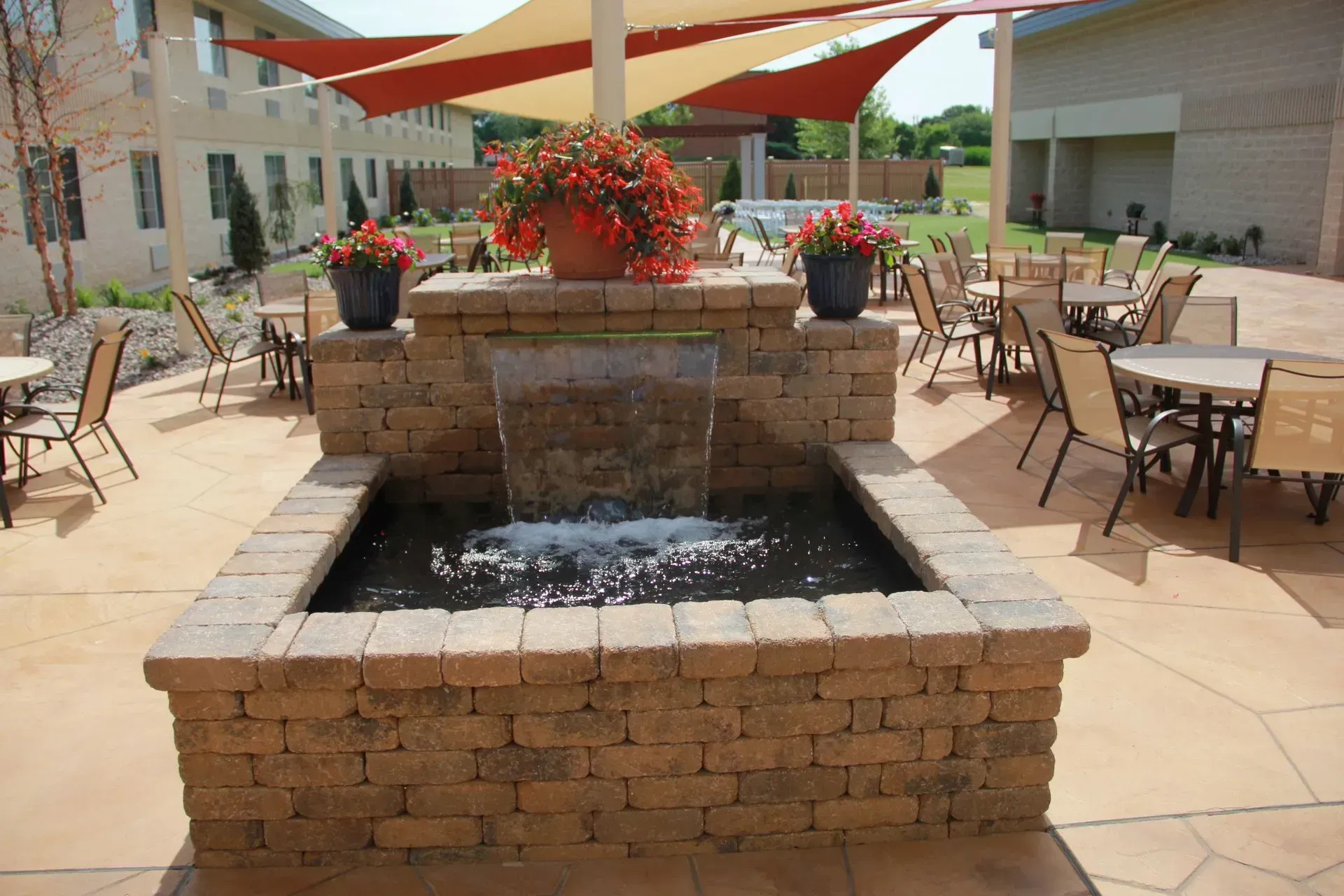 Outdoor patio with a brick fountain, flower pots, tables, and shade sails.