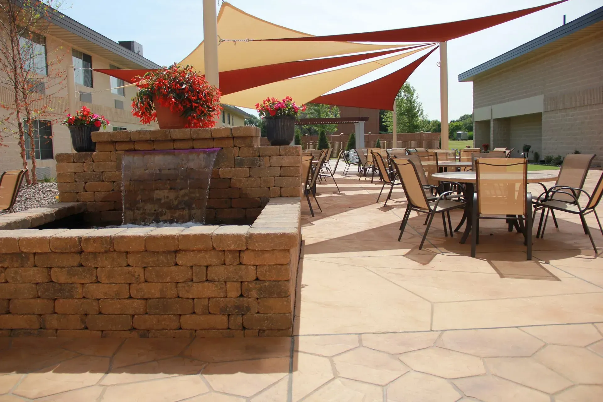 Outdoor patio with brick fountain, tables, chairs, and shade sail.