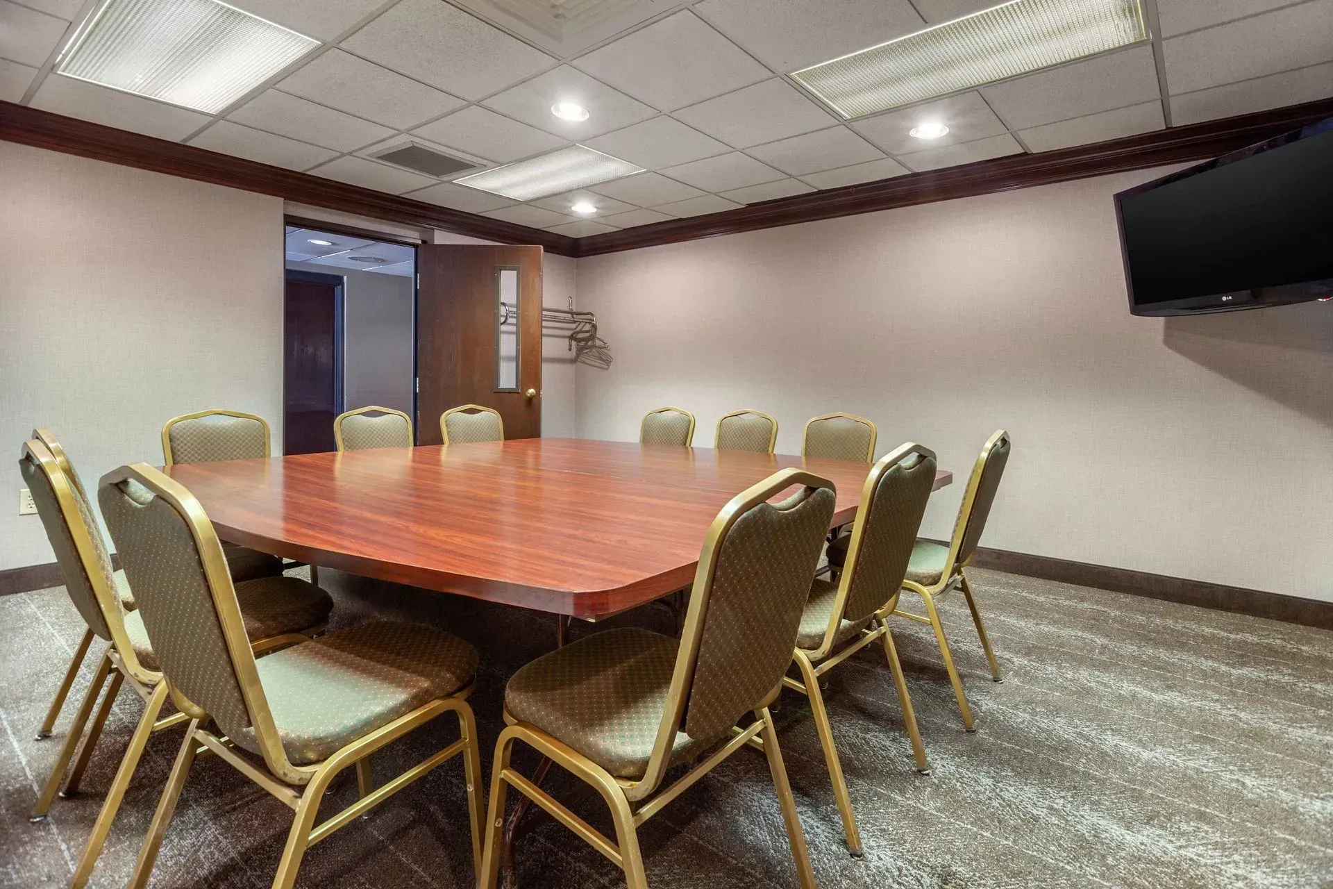 A meeting room with a large wooden table, chairs, and a TV on the wall.