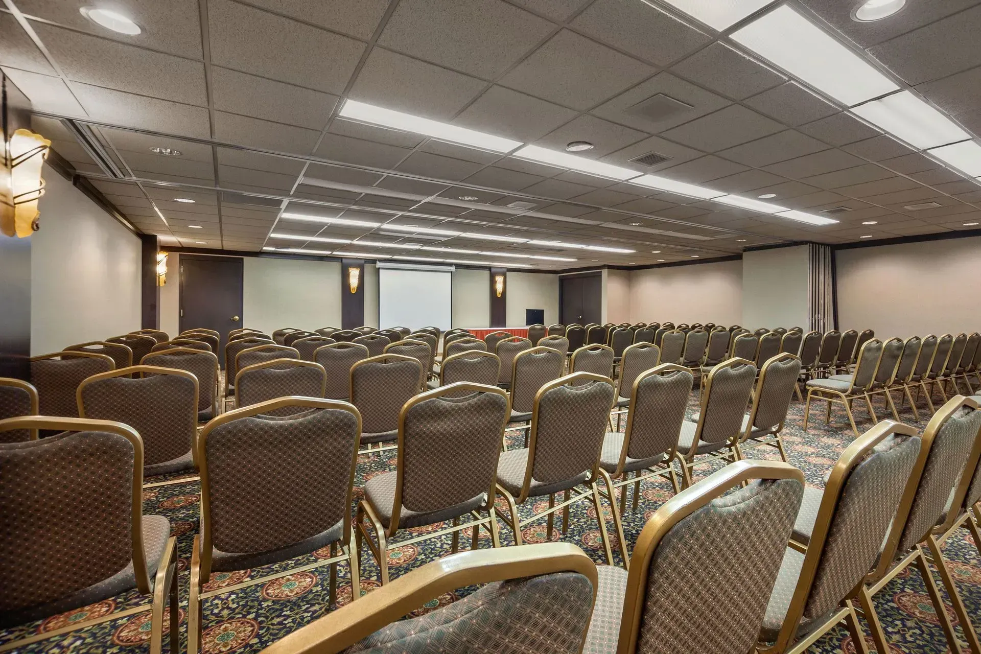Empty conference room with rows of brown chairs facing a projection screen.