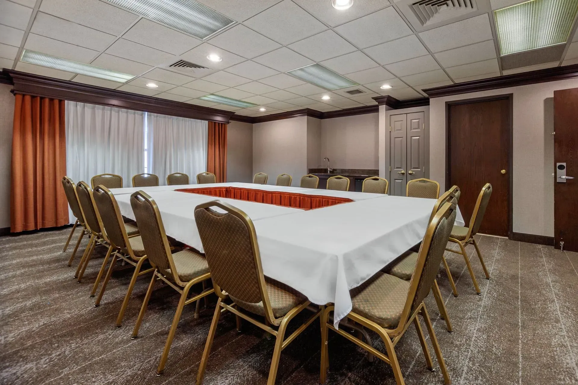 Conference room with rectangular table, chairs, neutral tones, and windows with curtains.