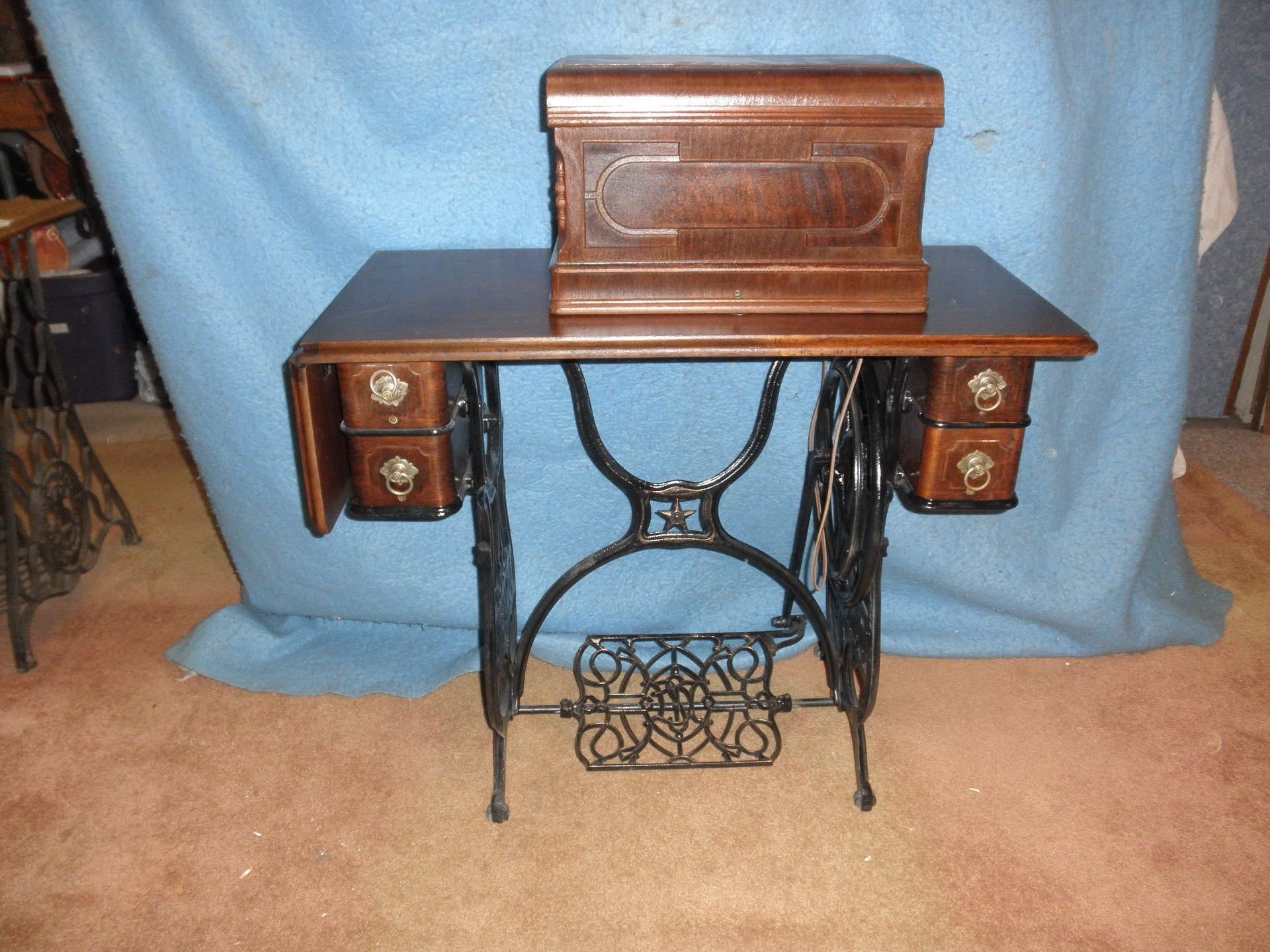 Antique sewing machine table with black iron base, wooden top, and matching cabinet on a blue backdrop
