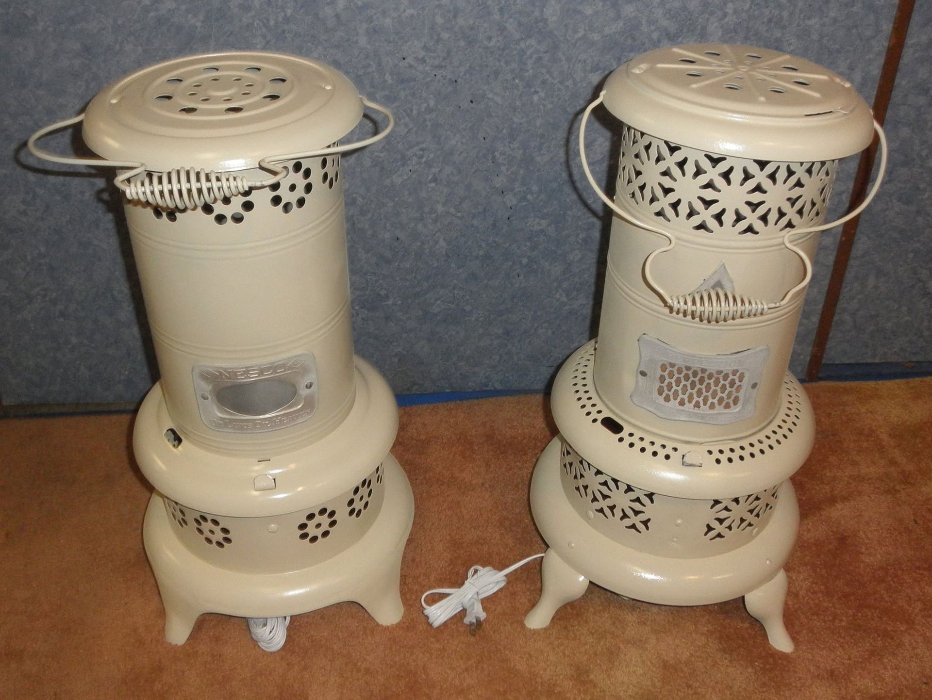 Two cream-colored electric space heaters on a wooden floor, each with a protective metal ring around the top.