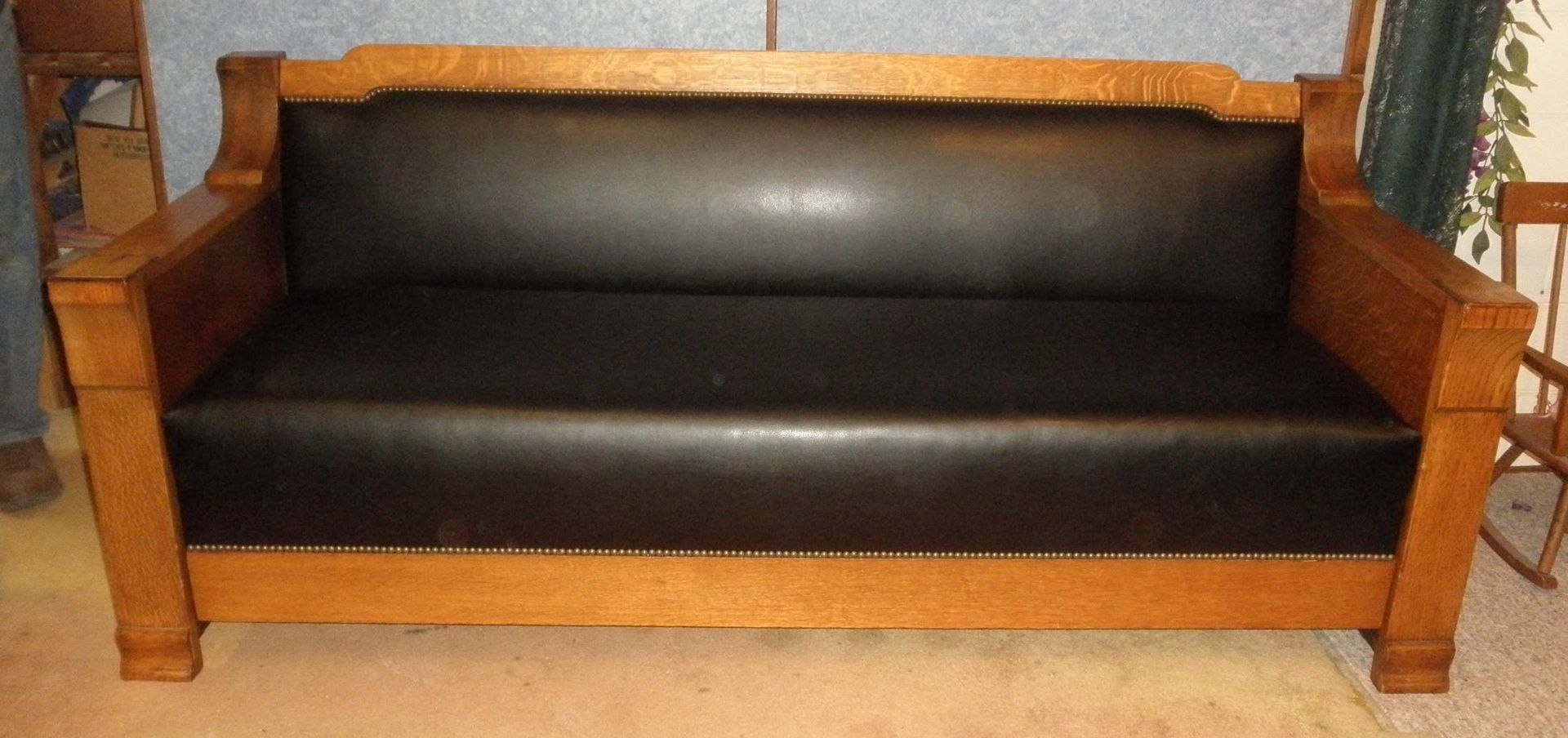 Wooden-framed black leather sofa with armrests against a wall
