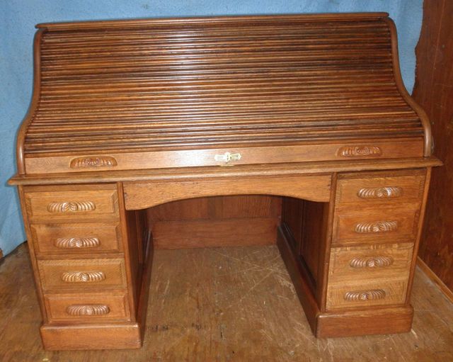 Wood-grain roll-top desk with drawers and open knee space against a blue backdrop