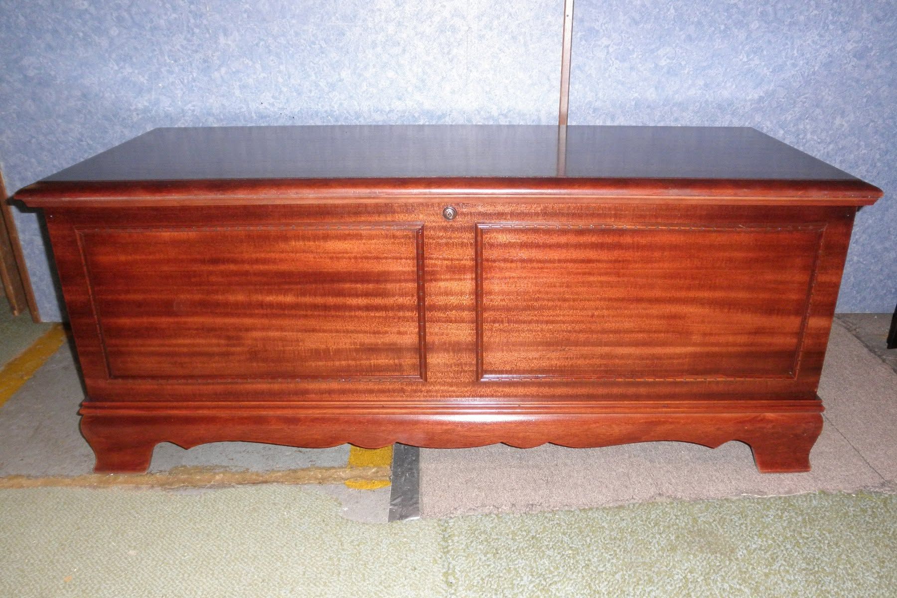 Wooden chest or storage bench with dark top and reddish front, standing on a carpeted floor