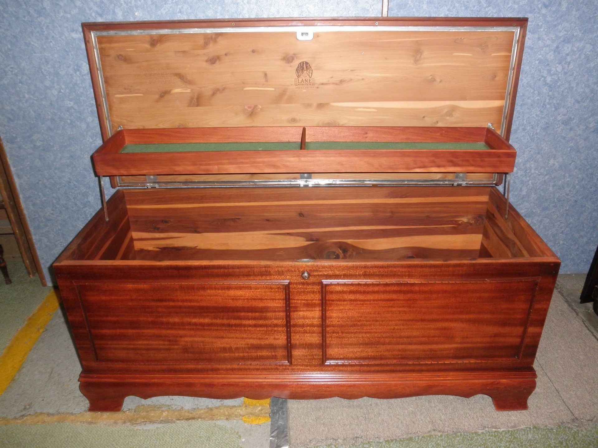 Open wooden chest with hinged lid and red interior, sitting on a floor.